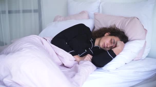 Portretul unei tinere care închide urechile cu pernă dimineața. Fata caucaziană se trezește din cauza zgomotului la domiciliu sau în camera de hotel . — Videoclip de stoc