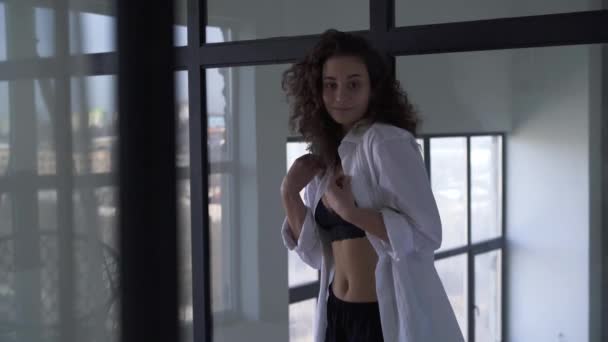 Porträtt av blyg vit flicka som visar spets behå under skjortan. Pinsam brunett kvinna poserar inomhus framför glasgarderoben. — Stockvideo