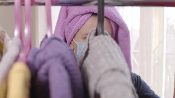 Close-up van Kaukasisch meisje in het gezicht masker kiezen van kleding achter kledingrek, het nemen van hanger en vertrek. Vrouwen levensstijl tijdens Covid-19 lockdown. Coronavirusinfectie, pandemie, mode. — Stockvideo