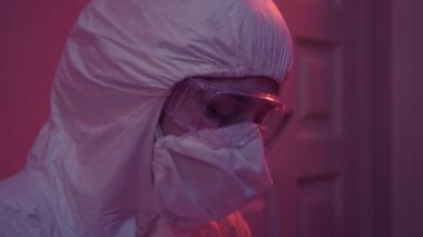 Aşırı çalışan, koruyucu takım elbiseli, gözlüklü, kafaya elle dokunan beyaz bir doktorun yakın çekimi. Coronavirus karantinasındaki yorgun sağlık çalışanının portresi. Covid-19 salgını, virolog.