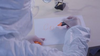 Koruyucu antiviral takım elbiseli bir sağlık görevlisi kağıda Covid-19 yazıyor. Küresel salgın, koronavirüs bulaşıcı hastalıklar, tecrit, karantina. Omzundan vuruluyor..