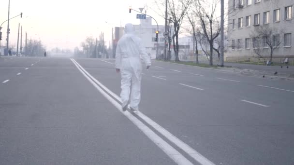 Gros plan de femme caucasienne positive en combinaison antivirale sautant sur la route de la ville vide pendant le confinement de Covid-19. Joyeux jeune fille qui s'amuse en quarantaine de coronavirus. Mode de vie, pandémie, loisirs . — Video