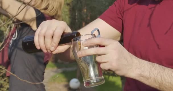 Close-up of senior Caucasian man pouring dark beer into glass and drinking beverage as woman cutting branches at the background. Adult couple taking care of garden in spring day. Cinema 4k ProRes HQ. — Stock Video