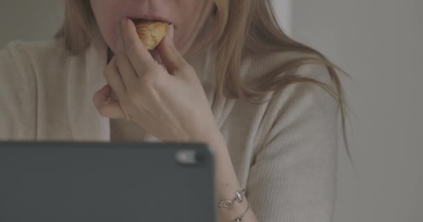 Extrême gros plan de femme blanche adulte mangeant un croissant savoureux devant la tablette. Une femme méconnaissable travaillant à distance à la maison. Mode de vie, freelance, isolement. Siège social Cinema 4k ProRes . — Video