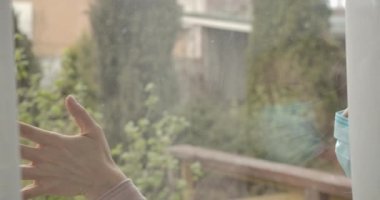 Karlı bir günde cam camına dokunan beyaz bir kadın. Covid-19 'un tecridi sırasında yüz maskesi takmış kimliği belirsiz üzgün bir kadın. Coronavirus salgını, karantina. Sinema 4k ProRes Merkezi.