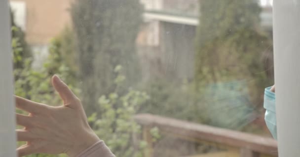 O femeie caucaziană atinge geamul într-o zi înzăpezită. O femeie necunoscută supărată în masca feței pe auto-izolare în timpul închiderii Covid-19. Pandemie de coronavirus, carantină. Cinema 4k ProRes HQ . — Videoclip de stoc
