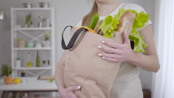 Femme caucasienne inconnue tenant sac à provisions avec des feuilles de salade fraîches, du pain et des fruits. Jeune femme méconnaissable posant avec une alimentation saine à l'intérieur. Mode de vie, végétarisme, cuisine . — Video