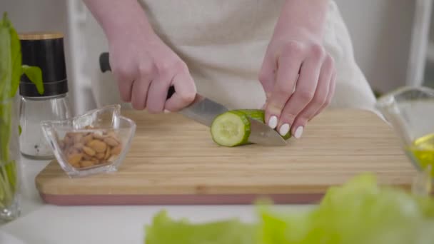 여자 손으로 도마 위에서 오이를 썰고 있습니다. 알아볼 수없는 젊은 백인 여성의 근접 사진 집이나 레스토랑에서 샐러드를 준비하고 있습니다. 건강 한 식사, 채식, 생활 양식. — 비디오