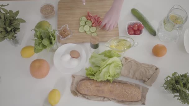 Ovanifrån av bord med matlagning ingredienser och kvinnliga händer skivning tomat på skärbräda. Ung okänd kaukasisk kvinna förbereder färsk ekologisk sallad till middag. Livsstil, kulinariska. — Stockvideo
