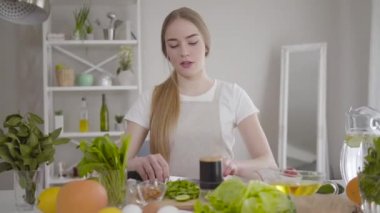 İçeride organik salata için malzeme kesen kendine güvenen beyaz bir kadının portresi. Güzel konsantre kız evde vegan yemeği pişiriyor. Sağlıklı yaşam tarzı, vejetaryenlik, sağlık.