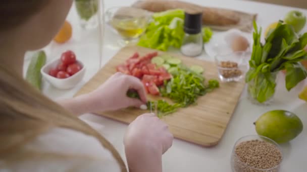 Giovane donna caucasica bionda che taglia ingredienti per l'insalata a bordo. Fiducioso chef che prepara piatti salutari. Sparare alle spalle. Stile di vita, attività di ristorazione, alimentazione sana . — Video Stock