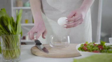 Bilinmeyen Kafkaseli kadın şeffaf kaseye yumurta kırıyor. Önlüklü genç bayan içeride yemek pişiriyor. Mutfak, mutfak, ev yapımı gıdalar, sağlıklı beslenme, yaşam tarzı..