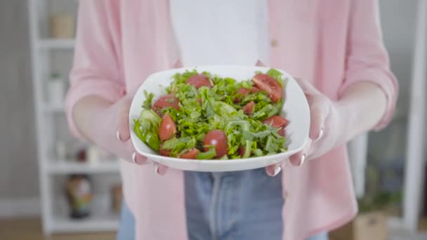 Eine unkenntliche Kaukasierin zeigt vor laufender Kamera frischen, schmackhaften Salat. Weibliche Hände halten Schüssel mit veganem Bio-Gericht aus Tomaten, Gurken und Grün. Vegetarismus, gesunde Lebensweise. — Stockvideo