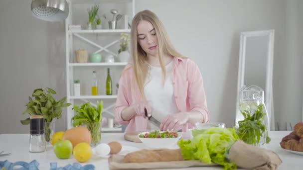 Porträtt av positiva kaukasiska flicka skivning tomater på skärbräda och dans. Leende kvinna njuter av matlagning hemma. Glädje, lycka, hälsosam kost, livsstil. — Stockvideo