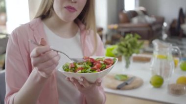 Tanınmayacak kadar güzel bir kız taze organik salatanın tadını çıkarıyor. Sağlıklı vejetaryen yemeği yiyen sarışın, beyaz bir kadın. Ağırlık kontrolü, güzellik, vejetaryenlik, sağlıklı yaşam tarzı..