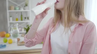 Beyaz şişeden yoğurt içen ve kameraya gülümseyen tanınmamış beyaz kadın. Sıska genç kız organik detoks yemeği yiyor. Sağlıklı içki, sağlıklı yaşam tarzı, keyif..