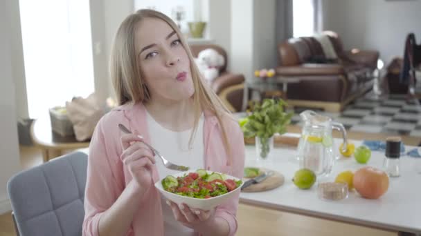 正の若い女性はおいしい有機サラダを噛むとカメラで笑顔.健康的な野菜料理を食べる喜びのブロンドの女性の肖像画。健康的なライフスタイル、体重管理、美しさ. — ストック動画