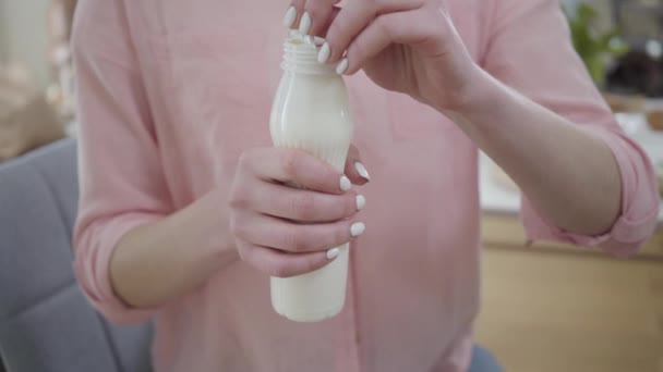 Primer plano de la joven mujer caucásica en camisa rosa abriendo botella blanca de yogur. Chica irreconocible sosteniendo productos lácteos saludables en las manos. Estilo de vida saludable, publicidad, estilo de vida . — Vídeo de stock