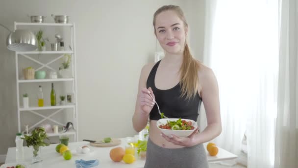 Красивая стройная белая девушка позирует с органическим салатом. Портрет веселой худой женщины в спортивной одежде, улыбающейся в камеру, держащей в руках вегетарианскую еду. Здоровый образ жизни, фитнес, контроль веса . — стоковое видео
