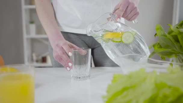 Närbild av kvinnliga händer häller infunderat detox vatten i dricksglas. Oigenkännlig passform Kaukasiska kvinna som tar hand om hälsa med cocktail av citroner, gurkor och örter. En hälsosam livsstil. — Stockvideo