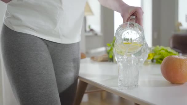 Onherkenbare jonge sportieve vrouw die water in glas giet. Slank blank meisje drinken geïnfundeerde cocktail. Gezonde levensstijl, metabolisme, hydratatie, gezondheidszorg. — Stockvideo