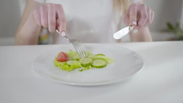 Крупный план неизвестной девушки, которая режет огурец ножом и вилкой и ест свежий органический салат. Молодая кавказка наслаждается вкусом вегетарианских овощей. Здоровый образ жизни, красота, благополучие — стоковое видео