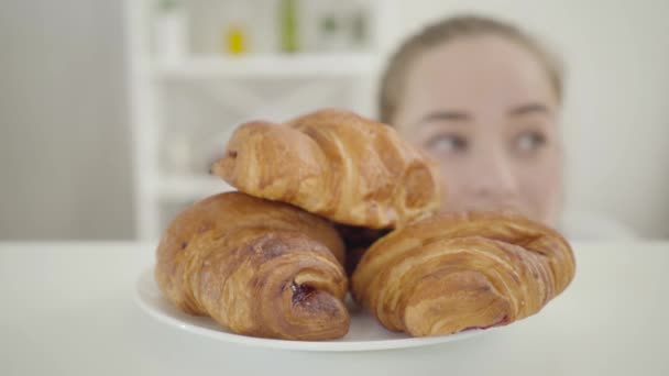 Θολή Καυκάσια κοπέλα κοιτάζει τριγύρω και δαγκώνει φρέσκο νόστιμο τραγανό κρουασάν. Νεαρή γυναίκα σπάει τη δίαιτα. Αυτοέλεγχος, απώλεια βάρους, ανθυγιεινή διατροφή, τρόπος ζωής. — Αρχείο Βίντεο