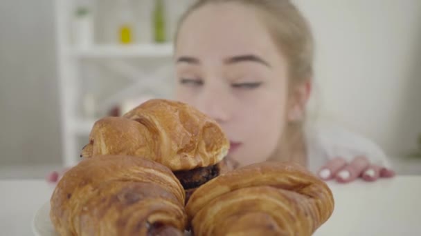 Portrét mladé hezké dívky, která jí čerstvý croissant. Zaměření změny z křupavé pekárny na tvář roztomilé kavkazské ženy porušuje dietu. Životní styl, strava, sebeovládání. — Stock video