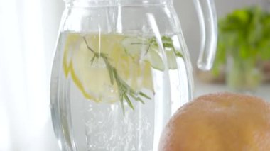 Şeffaf sürahiye aşılanmış bitkisel detoks kokteyli yakın plan. Cam kabın içine yavaş yavaş su dökülüyor. İçinde bitki, salatalık ve limon dilimleri var. Susuzluk, beslenme, refah, sağlıklı yaşam tarzı..