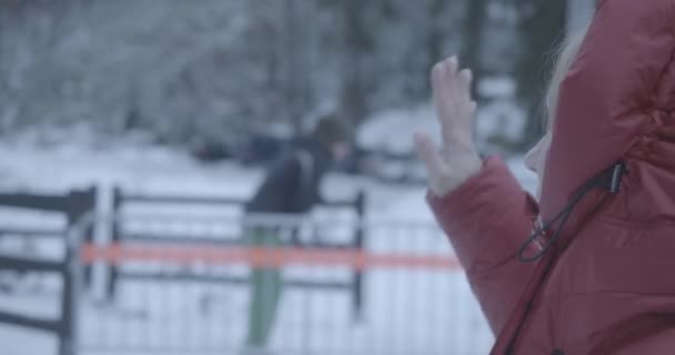 Close-up zijaanzicht van blonde blanke vrouw in winterjas zwaaiend naar onbekende skiër of snowboarder op skigebied. Volwassen dame rustend op vakantie buiten. Vrije tijd, levensstijl. Cinema 4k ProRes Hoofdkwartier. — Stockvideo