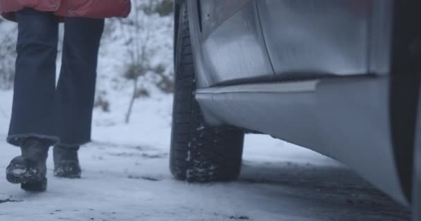 Vrouwelijke voeten in jeans en zwarte laarzen die naar de auto komen, sneeuw afschudden en in de auto stappen. Onherkenbare vrouw in voertuig op besneeuwde weg. Lifestyle, reizen. Cinema 4k ProRes Hoofdkwartier. — Stockvideo