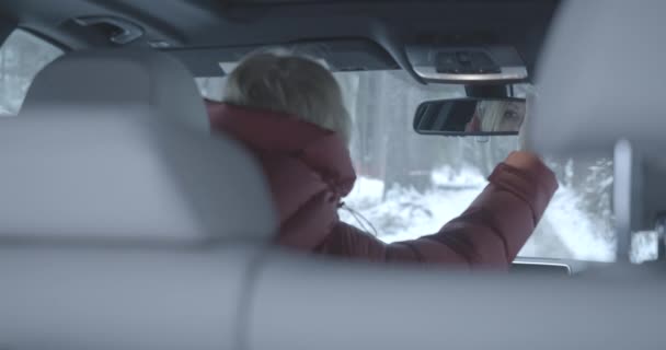 Beautiful blond Caucasian woman adjusting rearview mirror in automobile. Eyes of adult lady reflecting in mirror. Female driver sitting on drivers seat on snowy winter road. Cinema 4k ProRes HQ. — Stock Video