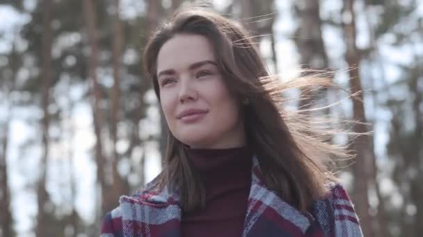 Portrait of confident brunette lady looking away and smiling as standing in forest in sunrays. Happy young woman with brown eyes spending sunny day outdoors on nature. Joy, leisure, lifestyle. — Stock Video