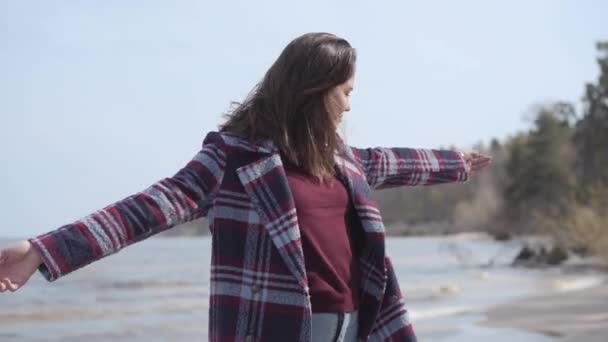 快乐美丽的高加索女孩站在河岸上举起双手。一个快乐的年轻女子在户外享受春日的画像。生活方式，休闲，千禧年，快乐. — 图库视频影像