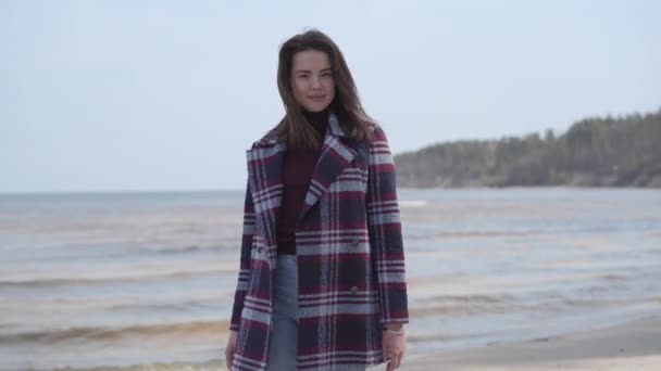 Portrait de jeune fille brune joyeuse marchant sur une plage de sable et souriant. Jeune femme blanche millénaire en veste à carreaux décontractée se promenant à l'extérieur. Mode de vie, joie, nature, loisirs . — Video