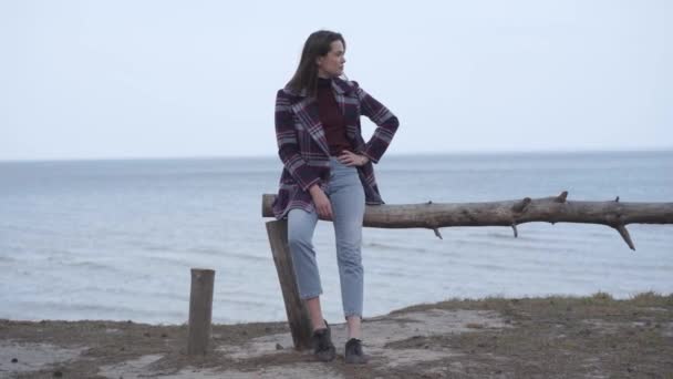 Portrait of confident brunette woman checking time on watch as sitting on log on riverbank. Beautiful Caucasian girl waiting outdoors. Lifestyle, punctuality, nature, confidence. — Stock Video