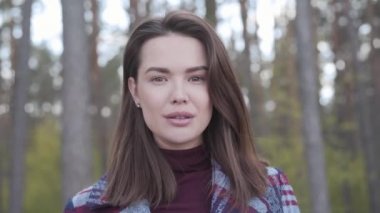 Güzel esmer kız kameraya bakıyor ve gidiyor. Güneşli ormanda kendinden emin beyaz bir kadının portresi. Boş zaman, doğa, yaşam tarzı, güven.