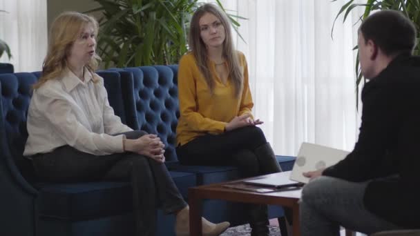 Porträtt av seriösa vita äldre och unga kvinnor som sitter på soffan och lyssnar på VD. Kollegor diskuterar lagarbete i avslappnad atmosfär. Företag, livsstil, jobb, framgång. — Stockvideo