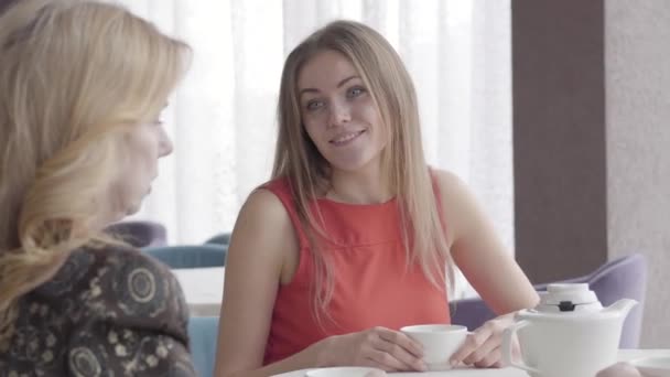 Portrait of young cheerful Caucasian woman laughing at jokes of senior lady in cafe. Beautiful brunette girl resting in restaurant with mother or elder friend. Joy, lifestyle, leisure, friendship. — Stock Video