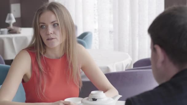 Portrait of serious Caucasian brunette woman talking to someone at the table in cafe. Unrecognizable man sitting at the foreground. Gorgeous businesswoman having break with colleagues in restaurant. — Stock Video