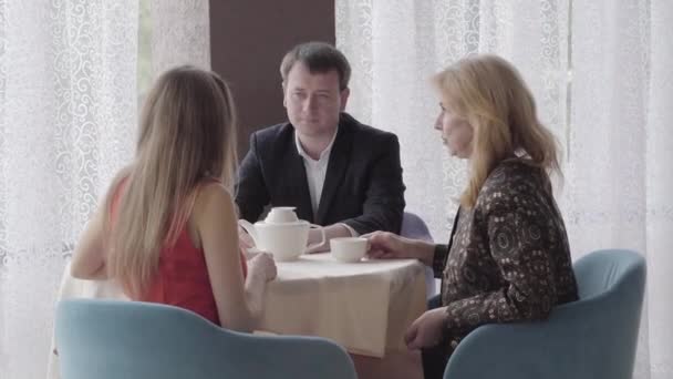 Portrait of cheerful adult Caucasian man enjoying meeting of mother and girlfriend in cafe. Young and senior ladies chatting and laughing in restaurant. Family, lifestyle, happiness, joy. — Stock Video