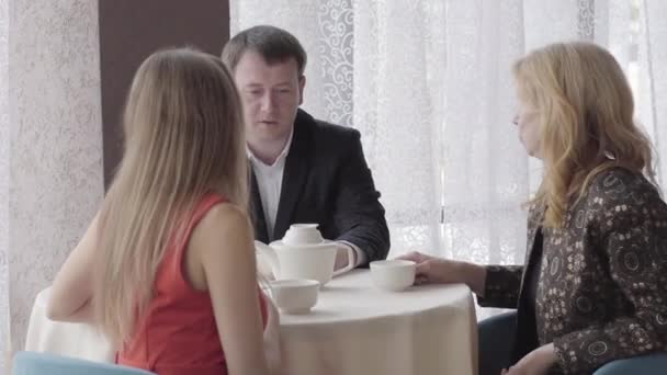 Молода жінка в червоному платті взяла трубку, сидячи з сім'єю в кафе. Кавказька дівчина дзвонить до ресторану. Ввічливість, спосіб життя, відпочинок. — стокове відео