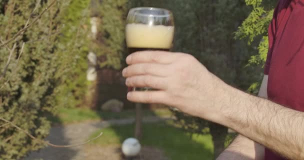 Close-up van een mannelijke hand die een glas donker schuimbier vasthoudt. Onherkenbare volwassen blanke man die buiten verse koude drank drinkt op zonnige lentedag. Cinema 4k ProRes Hoofdkwartier. — Stockvideo