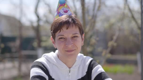 Portrait of smiling adult Caucasian woman in party hat toasting in online chat. Positive lady celebrating birthday of friend or colleague distantly. Covid-19 lockdown, coronavirus quarantine. — Stock Video