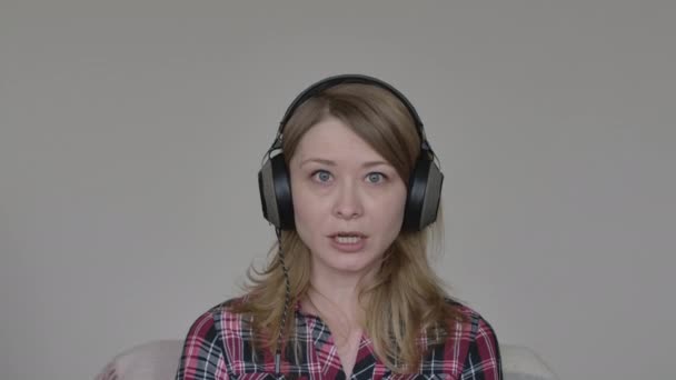 肯定的な若い女性の感情的にカメラで話しています。オンライン会議で何かを説明するヘッドフォンで金髪の白人の少女の肖像画。Covid-19パンデミックロックダウン無線ビジネスミーティング. — ストック動画