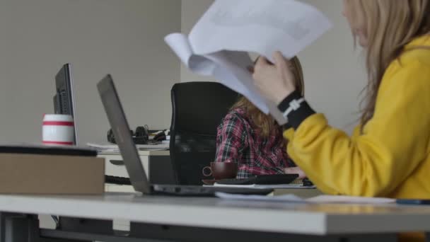 Two young Caucasian women sitting in office and discussing something. Lady in front sneezing as looking through documents. Business, job, lifestyle, overworking. Focused at background. — Stock Video