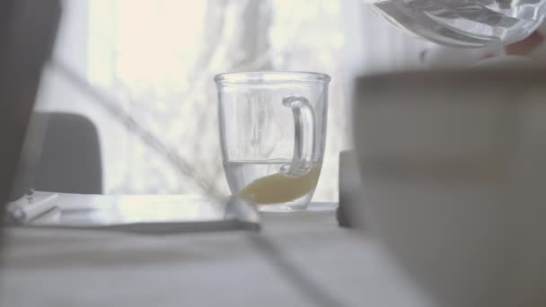 Наливаємо воду в прозору чашку з лимоном. Невідома людина додає рідину в склянку з цитрусовими. Здоровий напій, спосіб життя, охорона здоров'я, дієта . — стокове відео
