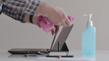Beyaz adam dezenfektanla tanınmaz hale geldi. Erkek eller akıllı telefonu, laptopu ve tableti dezenfektanla siliyor. Hijyen, dezenfeksiyon, Covid-19, koronavirüs, ilaç..
