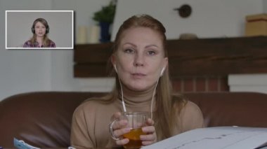 Cazibeli beyaz kadın çay içiyor ve kablosuz konuşmaları dinliyor. Covid-19 tecridinde genç bayanlar internette sohbet ediyorlar. Karantina, yaşam tarzı, iletişim, modern teknolojiler.