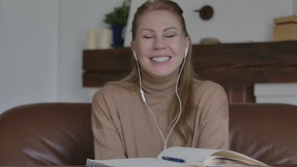 Portret van een vrolijke blanke vrouw in een oortelefoon die lacht en naar de camera kijkt. Vreugdevolle volwassen dame kijken online show of communiceren afstand en plezier hebben. Vrije tijd, levensstijl. — Stockvideo